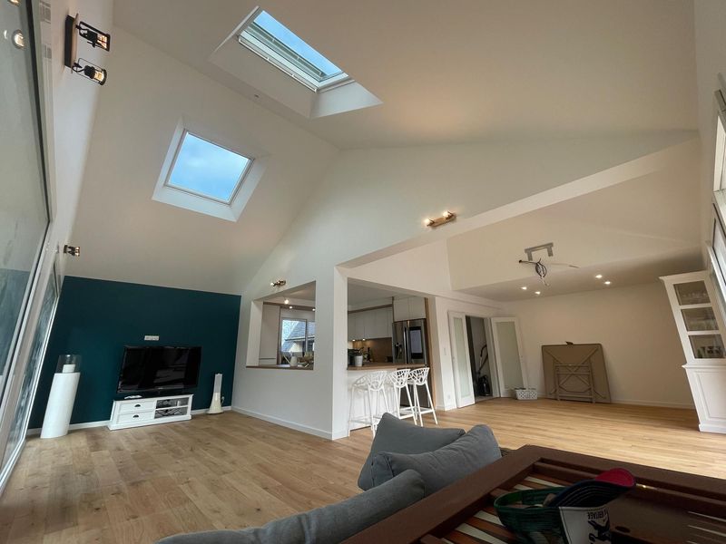 Un salon lumineux et moderne avec des plafonds mansardés, des puits de lumière, un mur d'accent turquoise et un agencement ouvert avec un sol clair.