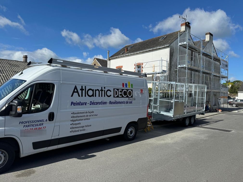 Une camionnette blanche Atlantic DECO garée dans la rue, tractant une remorque chargée d'éléments d'échafaudage pour une maison.