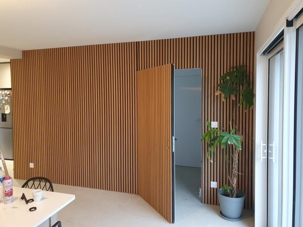 Dans une pièce moderne, un mur d'accent en lattes de bois dissimule une porte. Une plante en pot est posée sur le sol.