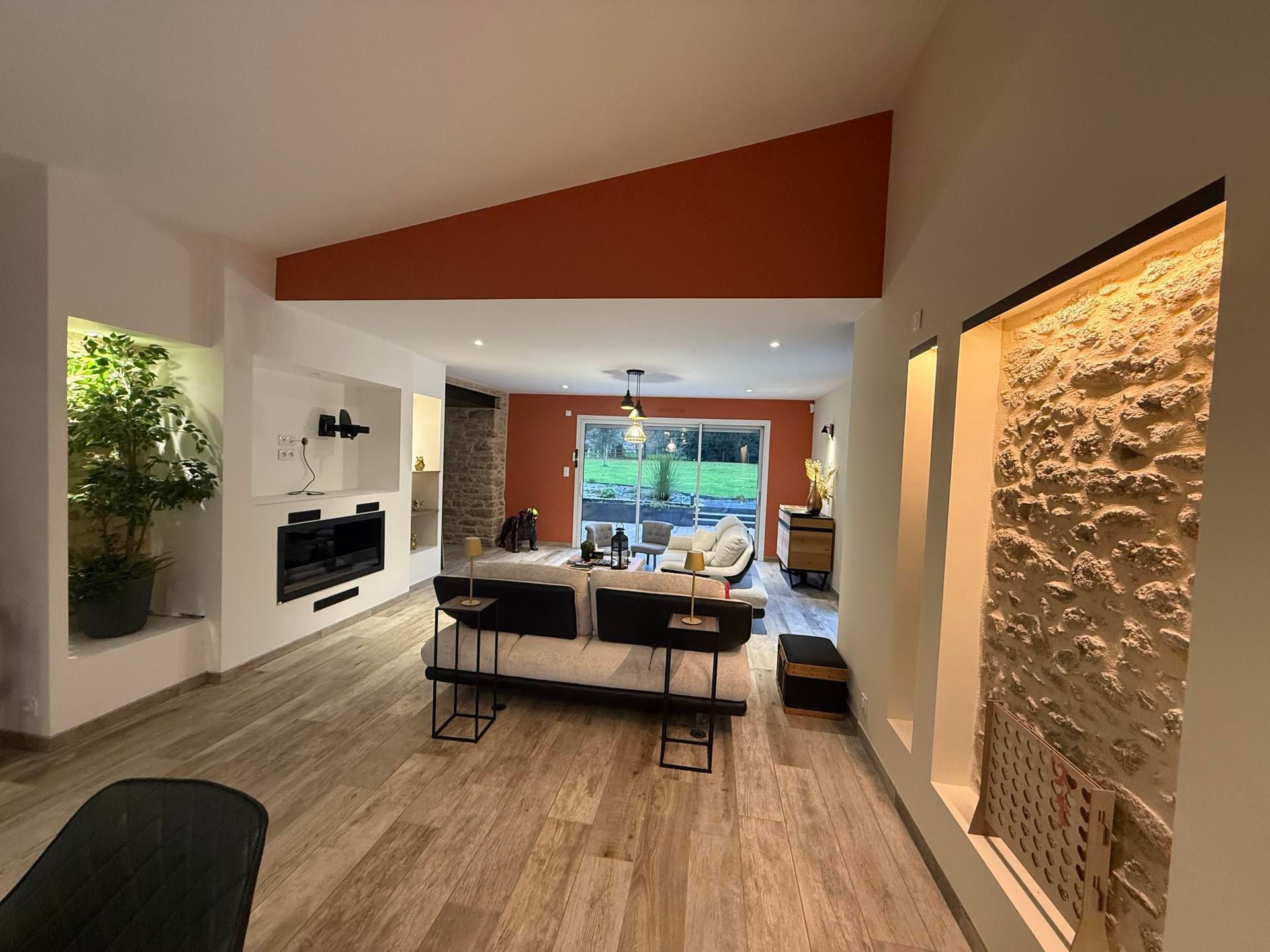 Salon moderne et ouvert avec parquet clair, canapé, accents muraux en pierre et un mur d'accent peint en orange.