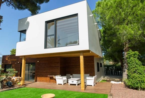 Casa moderna de dos pisos con nivel superior blanco, nivel inferior revestido de madera y patio de madera con asientos.