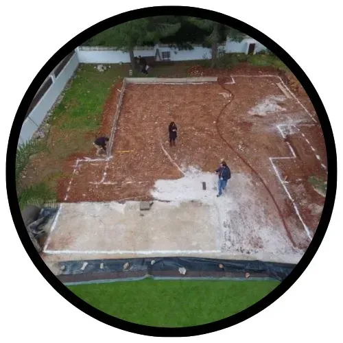 Sitio de construcción desde arriba con trabajadores; tierra, cimientos marcados y hormigón.