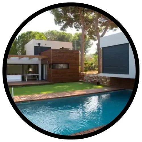 Casa moderna con piscina, terraza de madera y césped rodeado de árboles.