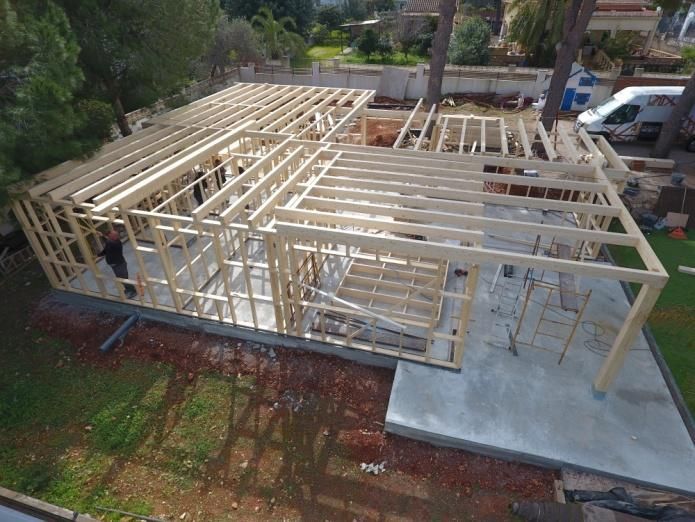 Estructura de madera de una casa en construcción sobre una base de hormigón, al aire libre con árboles.