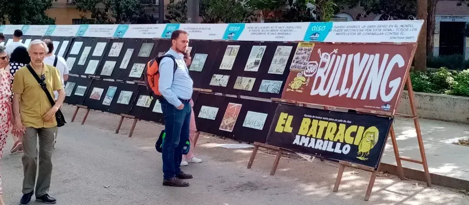Exposición al aire libre con grandes carteles y gente mirando una pancarta negra que dice “SOLVING” y “EL BARRIO”.