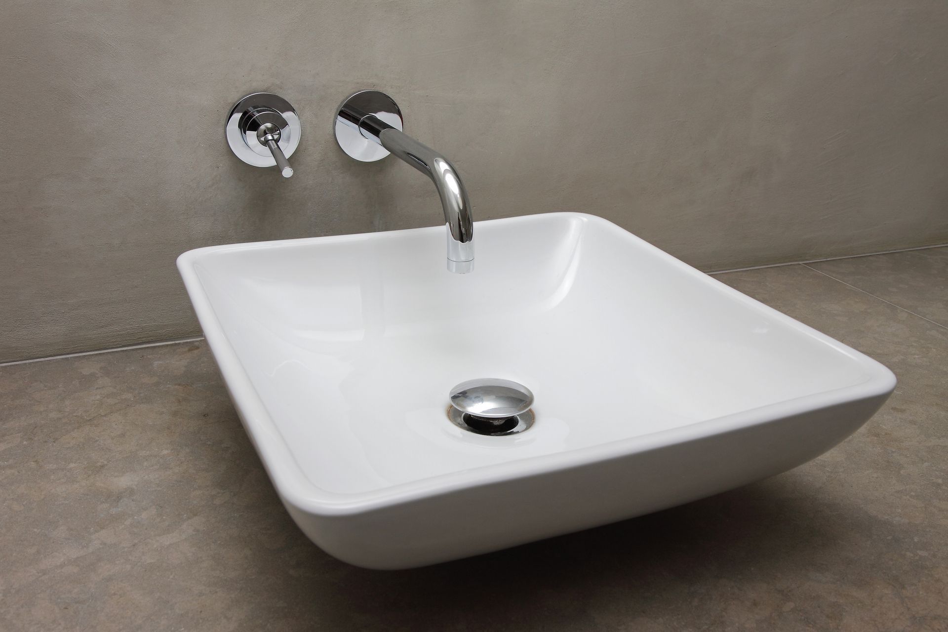 Lavabo carré blanc avec robinet et bonde chromés, fixé sur un mur gris.