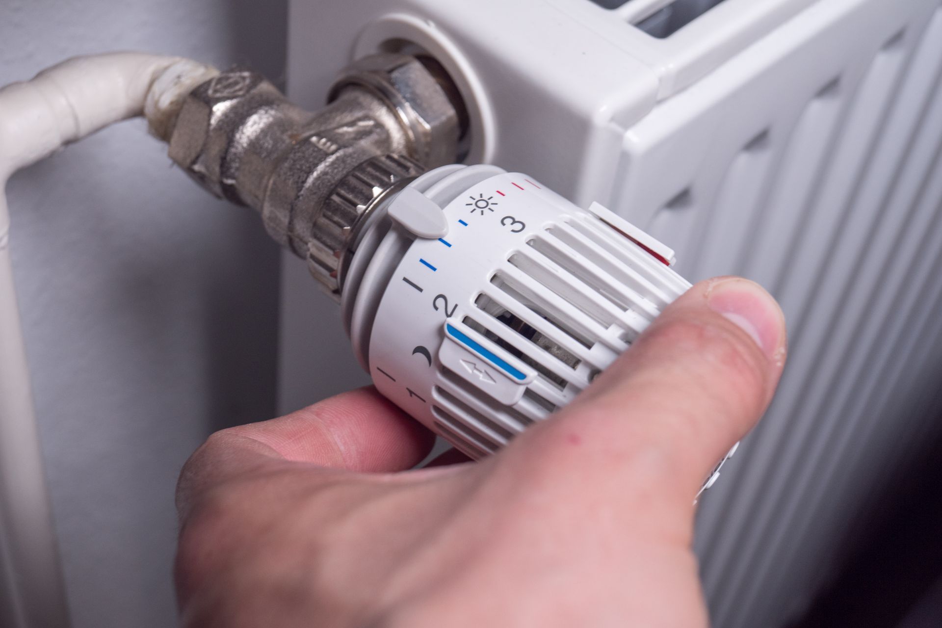 Une main tourne un robinet de radiateur blanc, ajustant le thermostat.