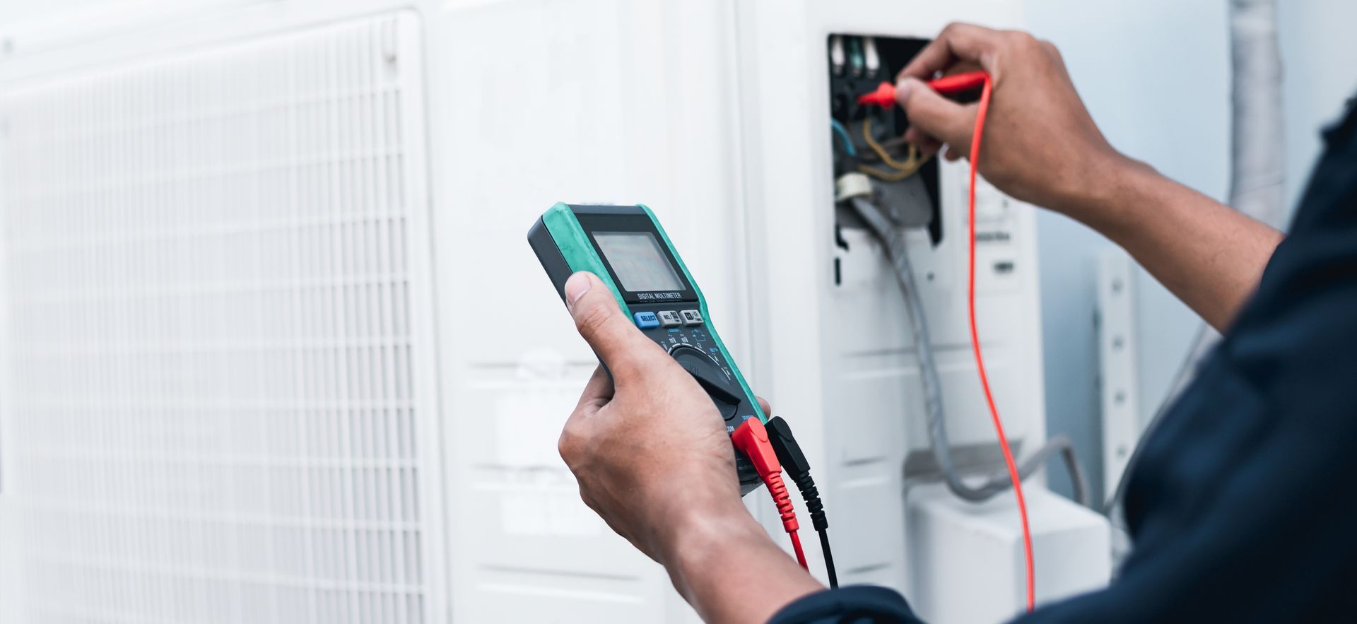 Une personne utilise un multimètre pour tester les composants électriques d'un climatiseur.
