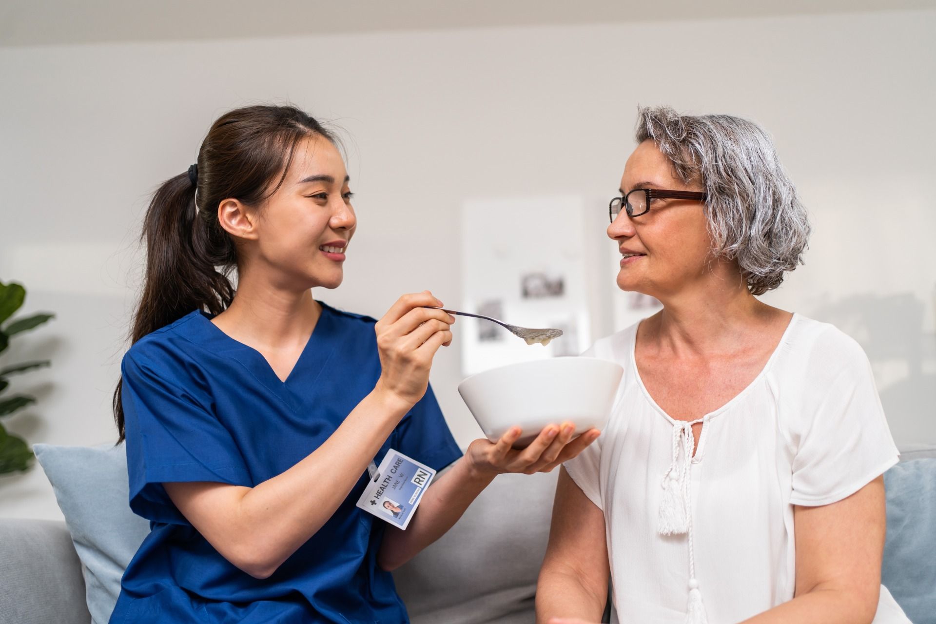 Eine Krankenschwester füttert eine ältere Frau mit einer Schüssel Essen.