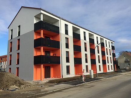Modernes Wohnhaus mit weißen, orangen und schwarzen Fassaden entlang einer Straße