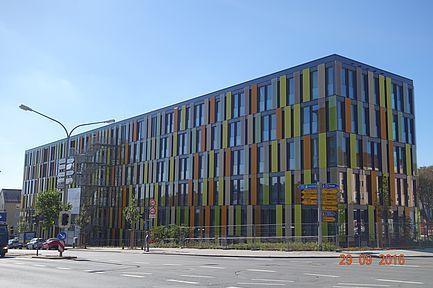 Modernes mehrstöckiges Gebäude mit farbenfrohen vertikalen Paneelen an einer sonnigen Straßenecke