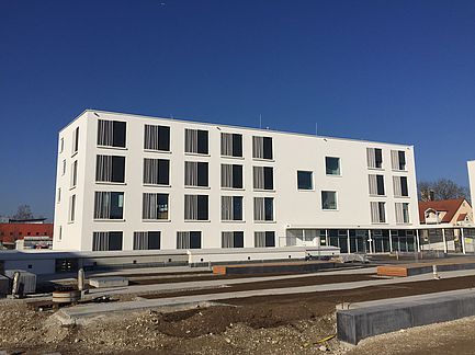 Modernes weißes Apartmentgebäude mit Balkonen unter einem klaren blauen Himmel