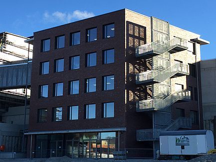 Modernes Backsteinbürogebäude mit gläsernem Treppenhaus und Fensterreihen im Tageslicht