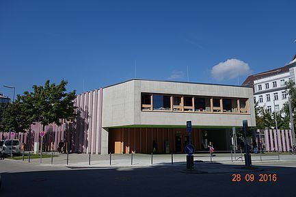 Modernes Gebäude mit geschwungener Fassade und Eingang unter klarem, blauem Himmel