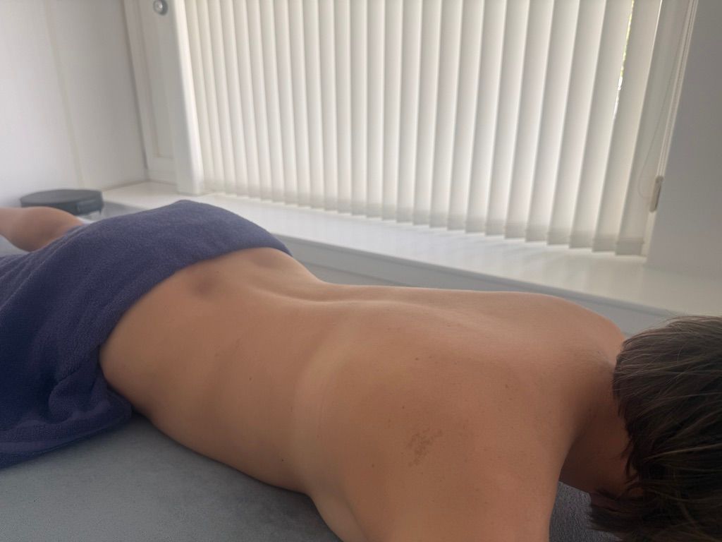 Ein Massagetherapeut übt Druck auf den Oberschenkel einer Person aus, während diese auf einer weissen Behandlungsliege liegt.