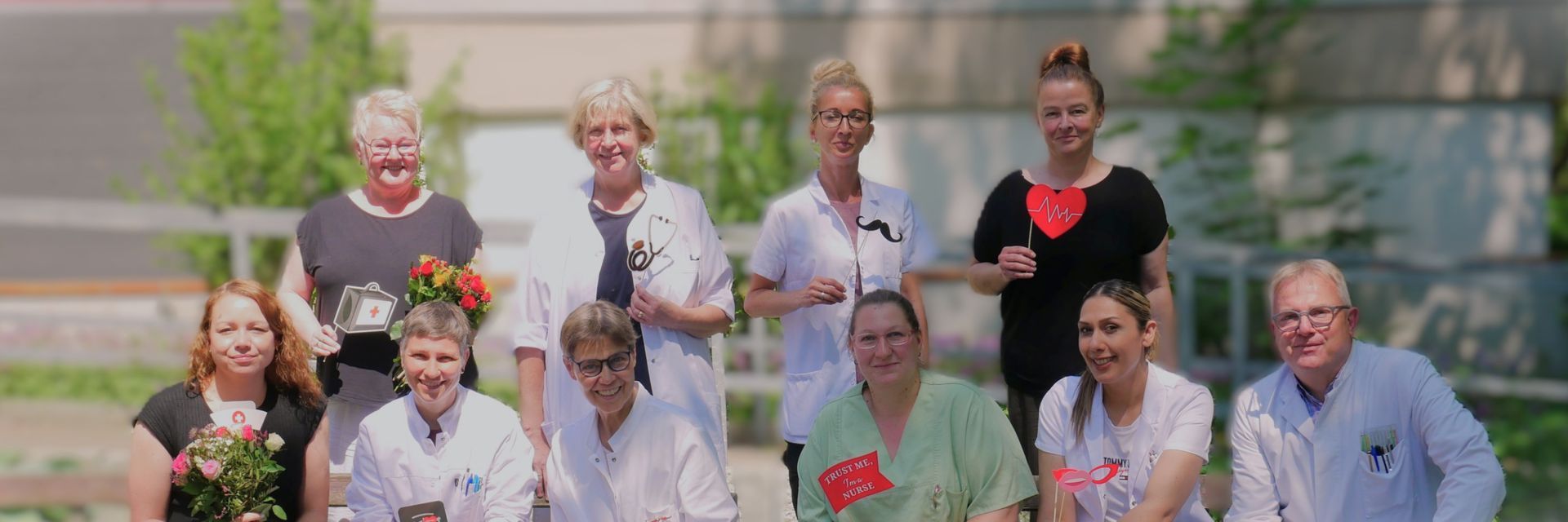 Eine Gruppe von Menschen posiert im Freien in einem Garten, hält Blumen in den Händen und lächelt in die Kamera.