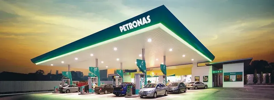 Um posto de gasolina Petronas com carros estacionados na frente.