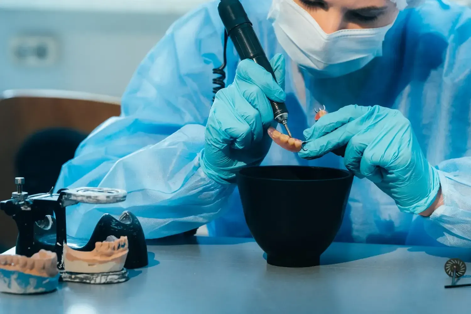 Un técnico dental con equipo de protección personal utiliza una pieza de
