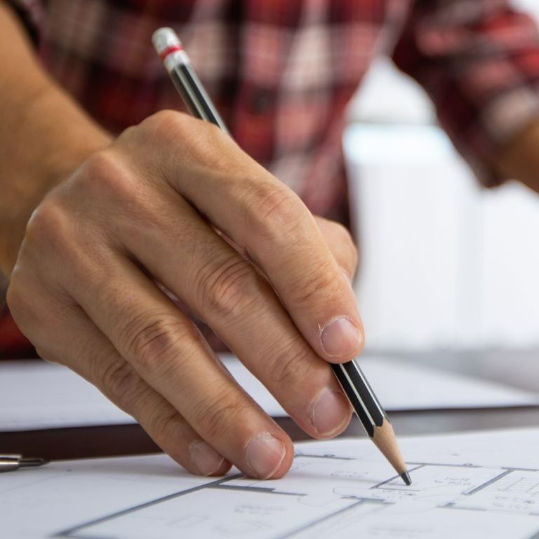 Une main montre un plan avec un crayon
