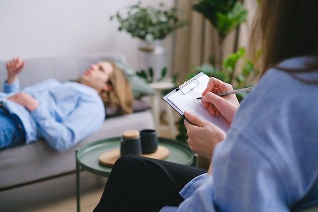 Una mujer está acostada en un sofá mientras otra mujer sostiene un portapapeles.