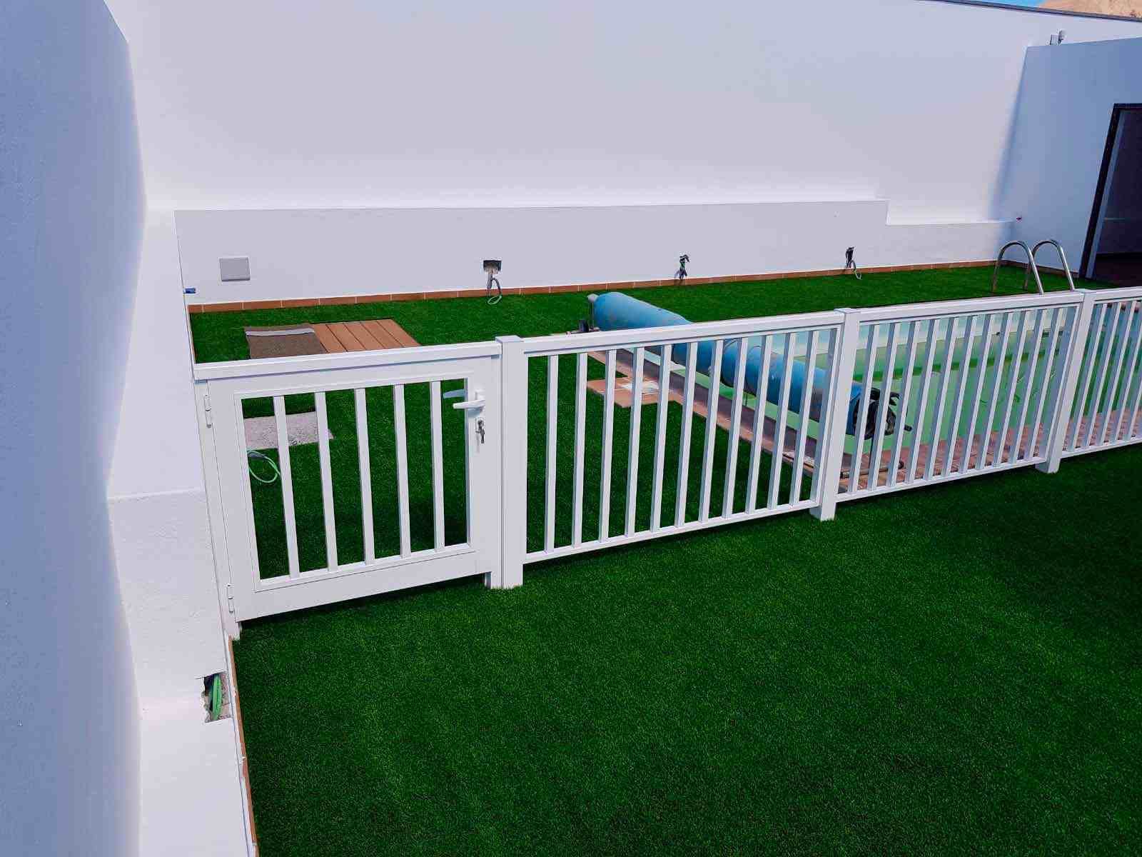 Una valla blanca rodea un exuberante césped verde junto a una piscina.