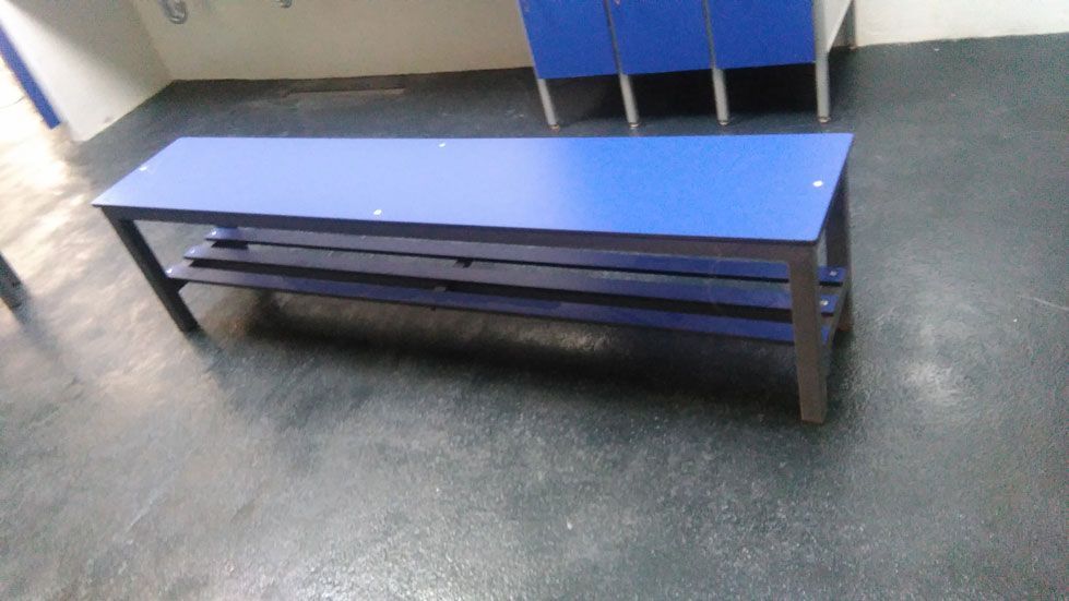 Un banco azul está sentado en un vestuario al lado de casilleros azules.