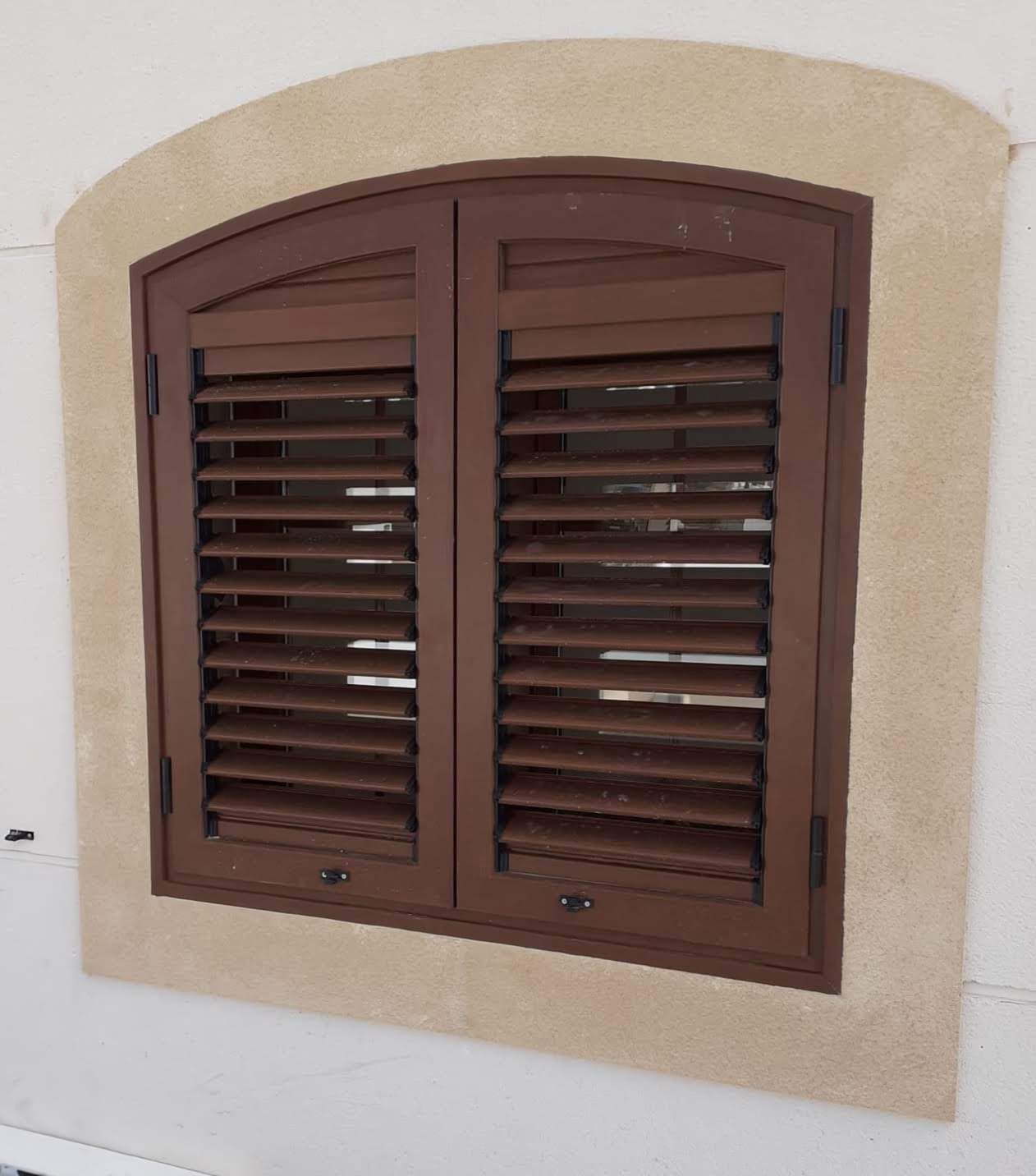 Una ventana con contraventanas arqueadas en una pared blanca