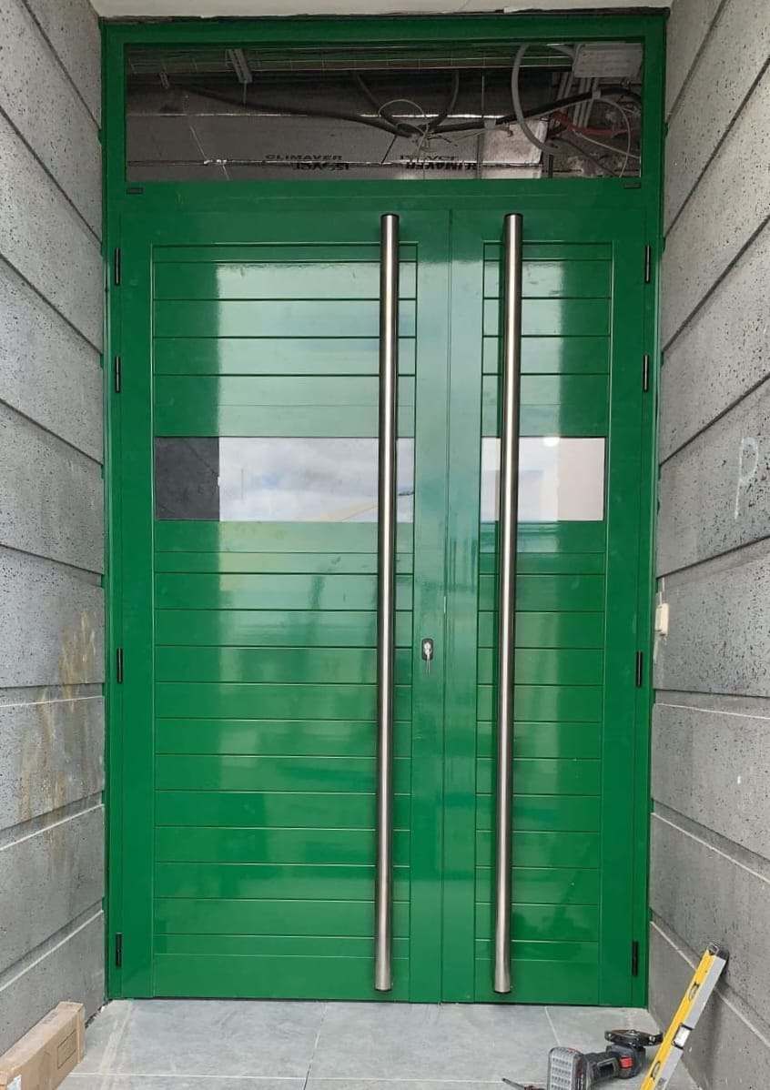 En un edificio hay una puerta verde con manijas de acero inoxidable.