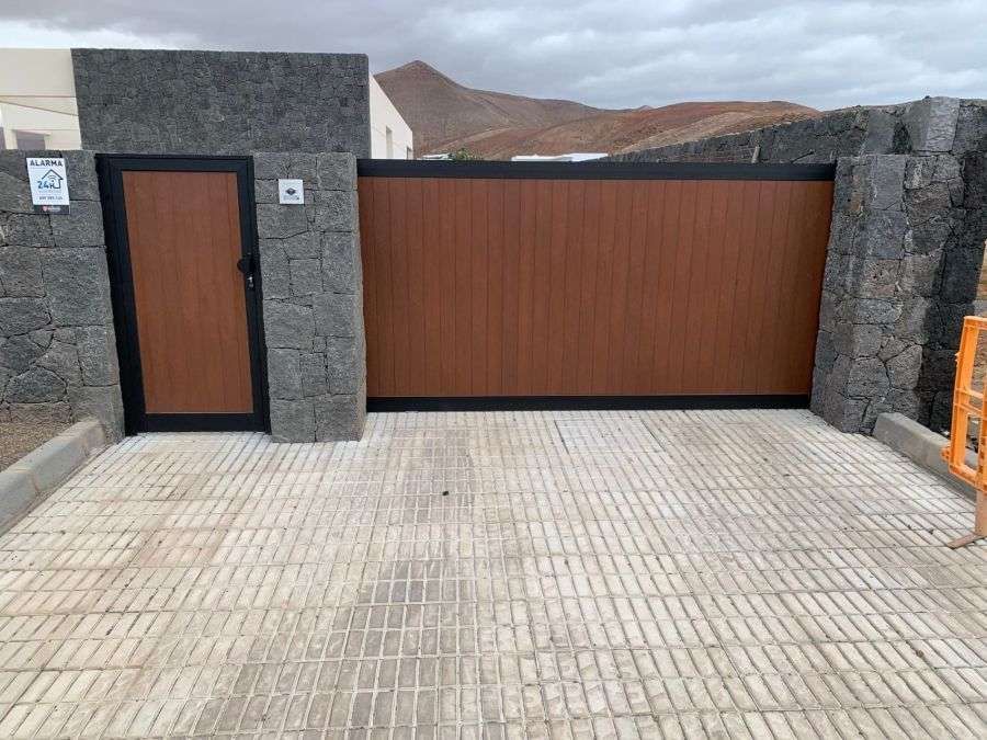 Una puerta de madera está rodeada por un muro de piedra y un camino de entrada de ladrillo.