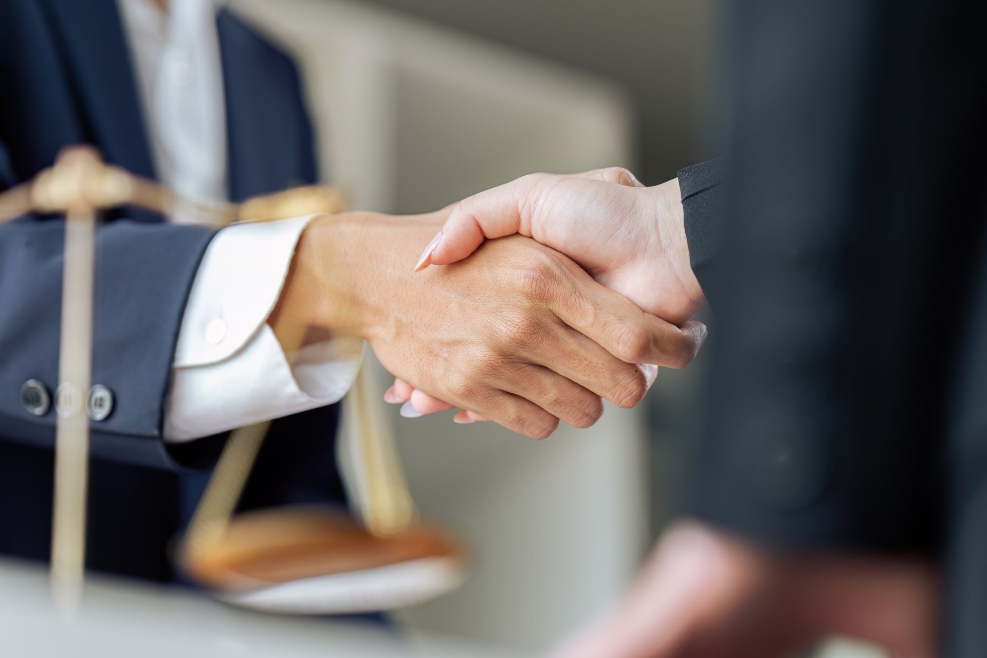 Une personne en costume serre la main d'une autre. On aperçoit la balance de la justice en arrière-plan.