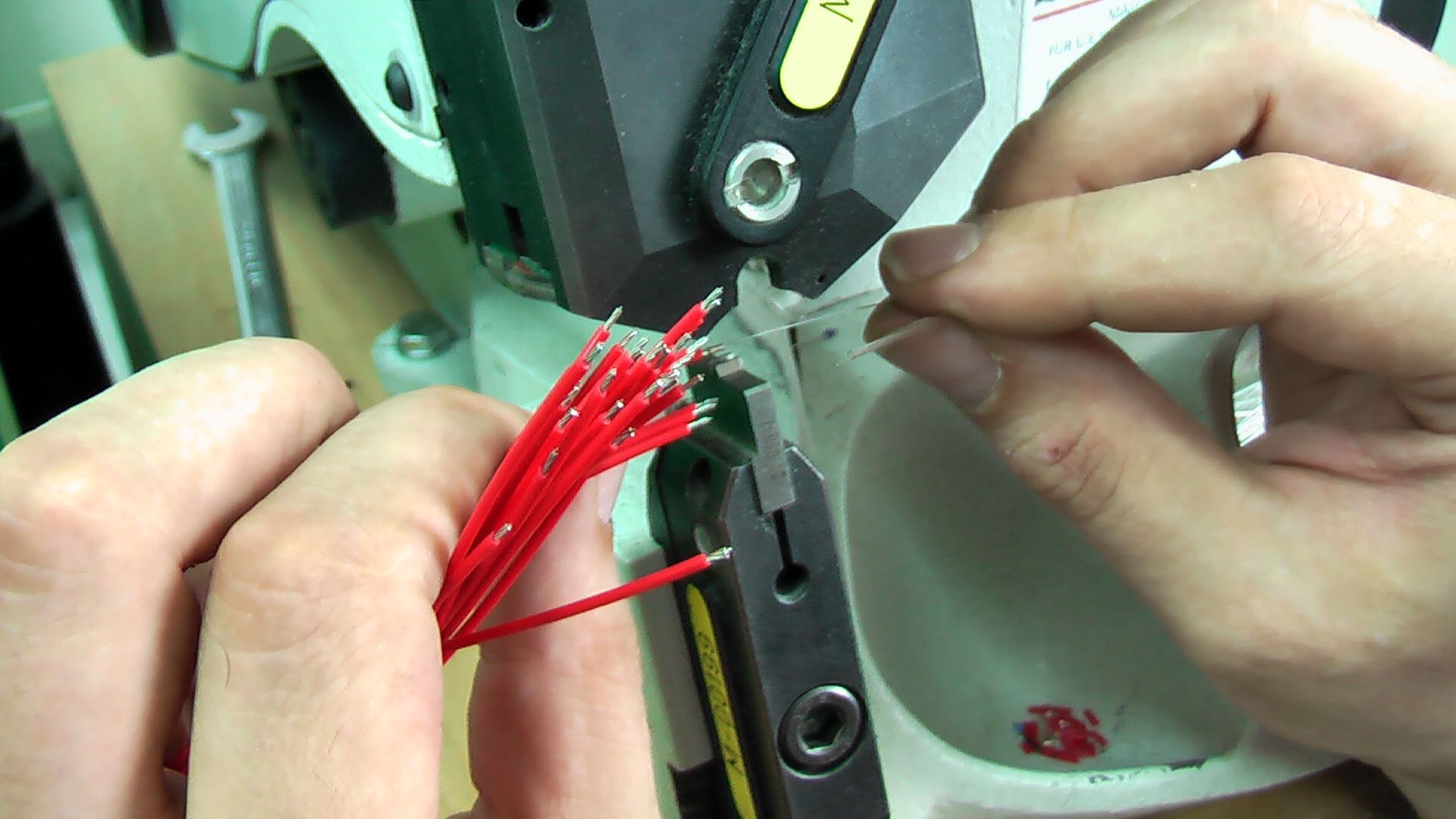 A person is holding a red wire in their hands in front of a machine.