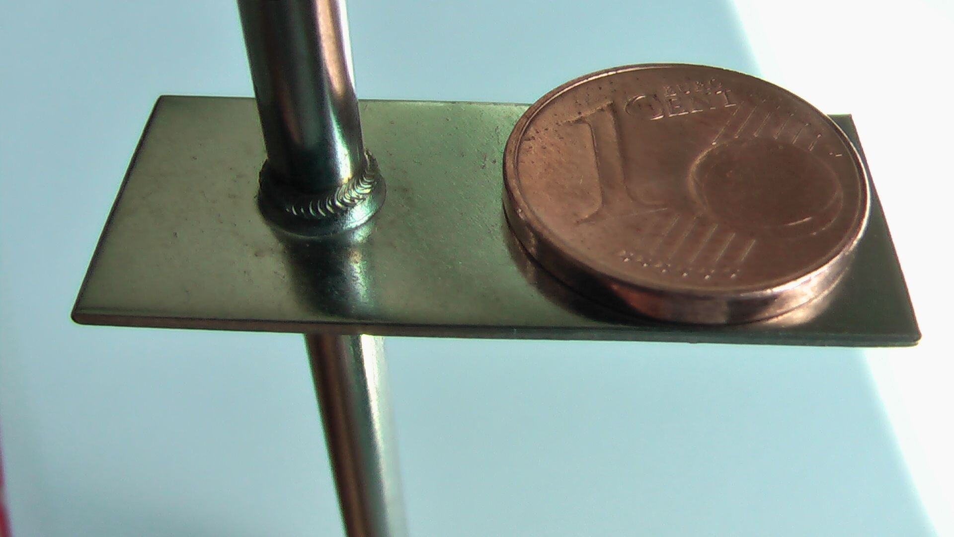 Eine 1-Cent-Münze liegt auf einem Stück Metall, um das Laserschweißen zu demonstrieren.