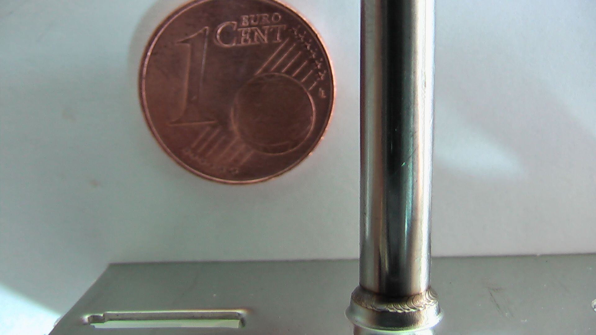 Eine 1-Cent-Münze liegt neben einem Metallgegenstand um das Laserschweißen zu demonstrieren.