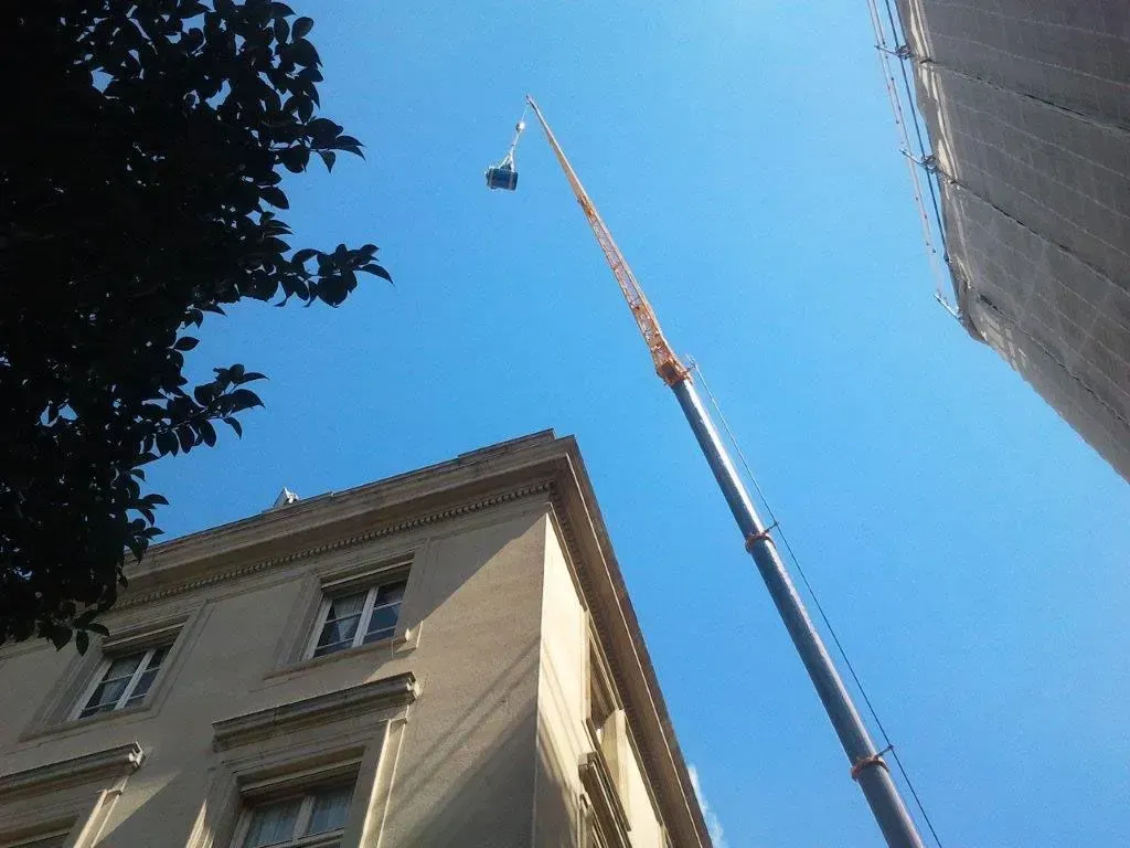 Une grue se dresse au-dessus d'un immeuble beige à plusieurs étages.