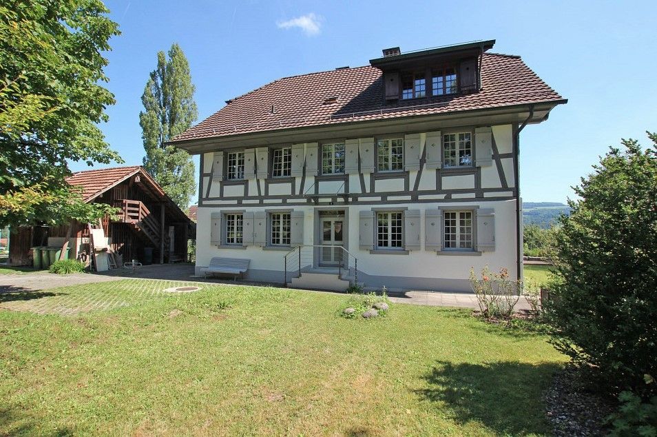 Ein großes weißes Haus mit einem braunen Dach steht mitten auf einer Wiese