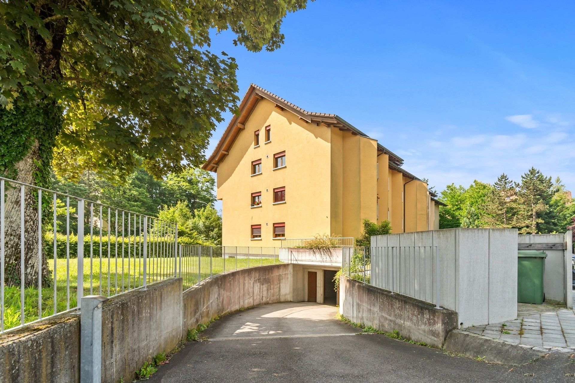 Ein gelbes Gebäude ist von Bäumen und einem Zaun umgeben