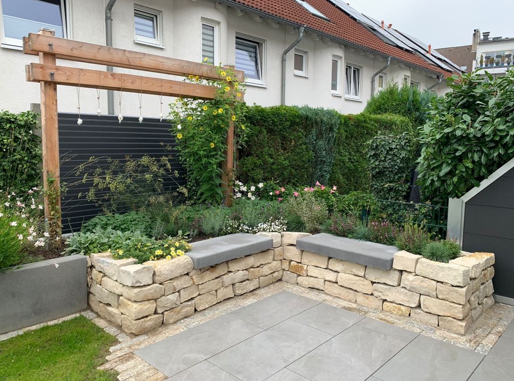 Garten im Freien mit Steinsitzgelegenheiten, Pergola und üppigem Grün.