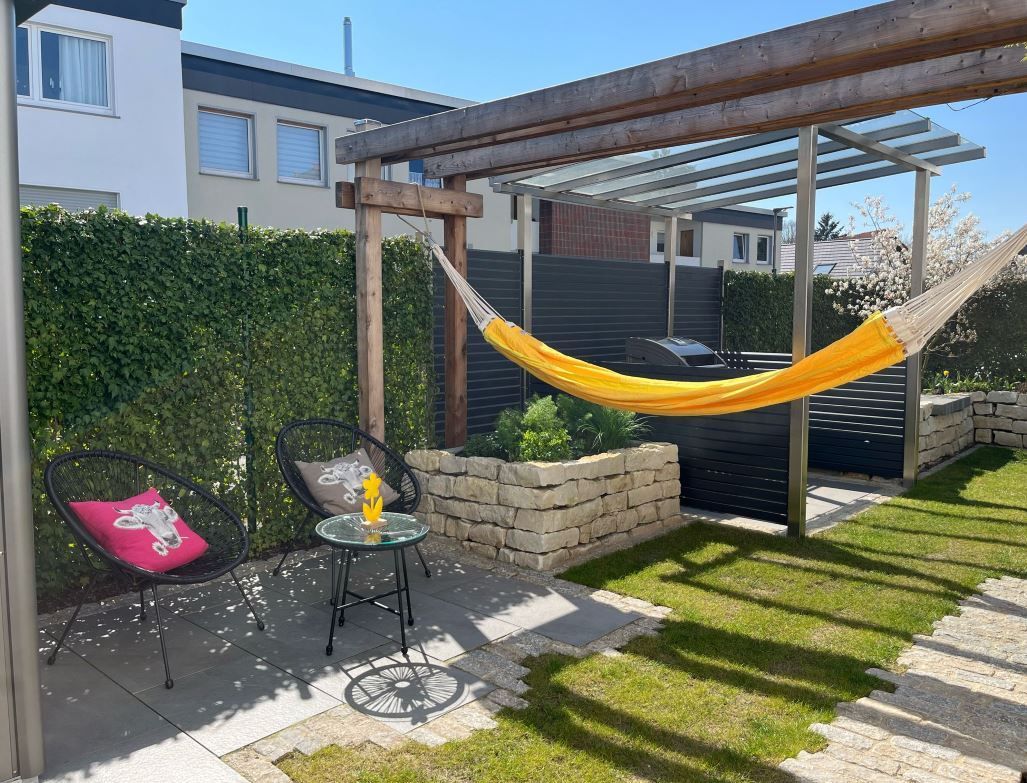 Hinterhof mit einer gelben Hängematte, einem kleinen Tisch, zwei Stühlen und einem kleinen gemauerten Pflanzkübel.