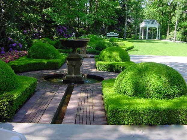 Formaler Garten mit terrassenförmigen, grünen Hecken, Springbrunnen und einem Pavillon in der Ferne.