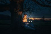 Eine Person liest nachts unter einem Baum, der von sanftem Licht erhellt wird, ein Buch.