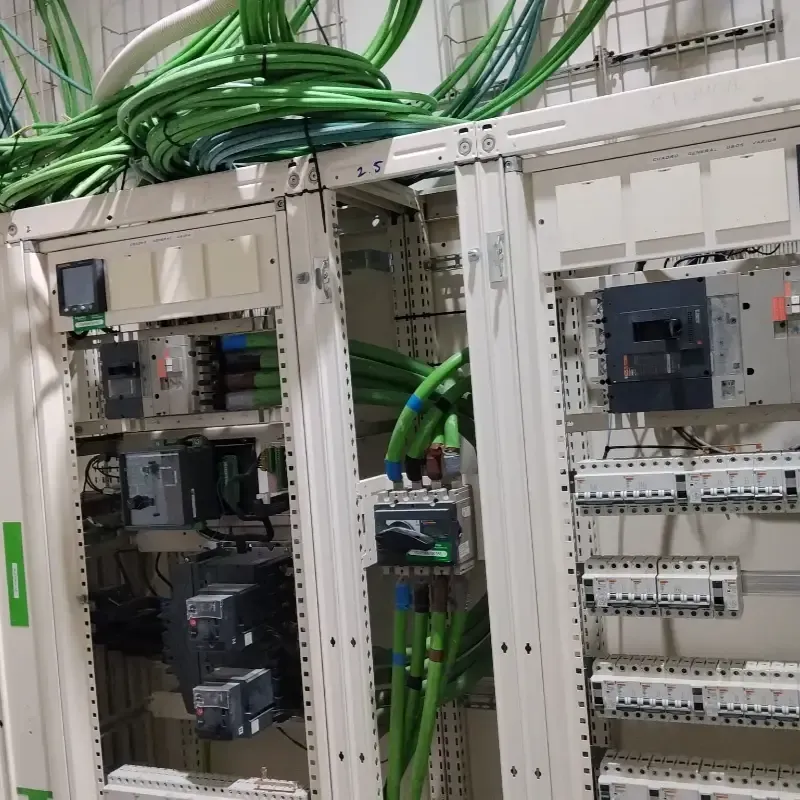 Armario de control eléctrico con cables verdes y componentes industriales dentro de una carcasa abierta.