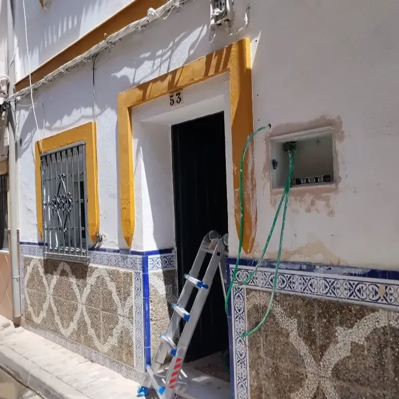 Exterior de una casa con puerta abierta, ventana, escalera y panel eléctrico montado en la pared en reparación.