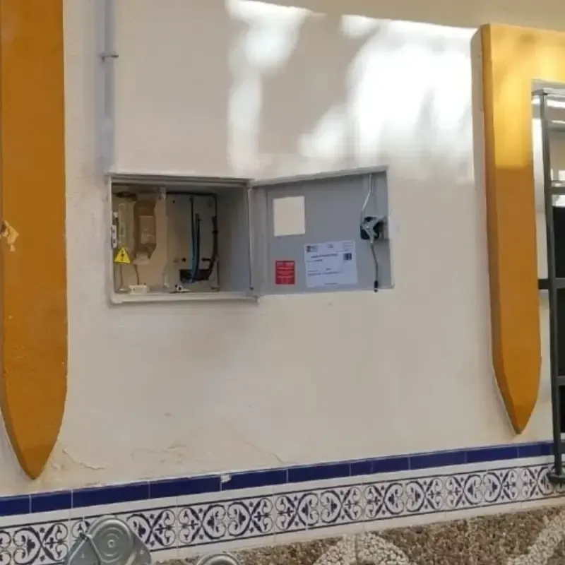 Panel eléctrico abierto en una pared blanca, con molduras de azulejos azules estampados debajo.