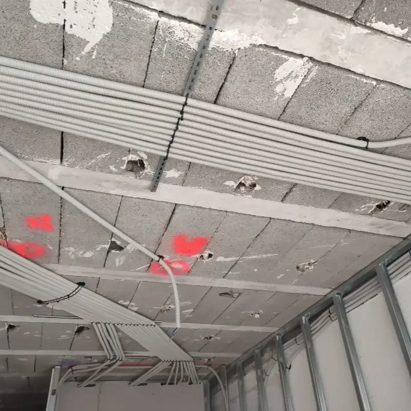 Techo parcialmente terminado con cableado expuesto, paneles grises y marcas de pintura roja en una obra en construcción.