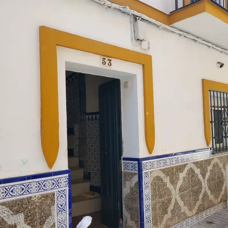 Puerta blanca con detalles amarillos y fachada de azulejos azules estampados, número 53 sobre la entrada.