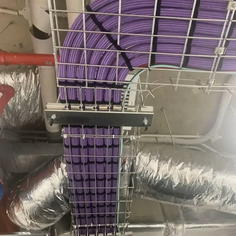Cables morados tendidos a través de una bandeja metálica portacables en un entorno industrial.