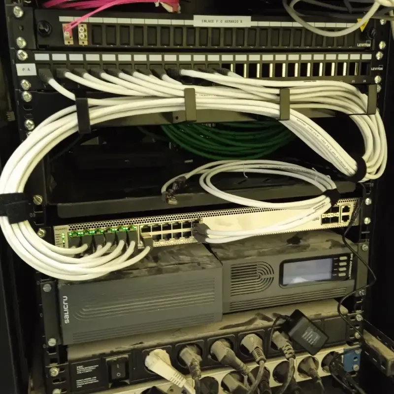 Rack de red con cables blancos y verdes, conmutadores y equipos apilados en un armario para servidores.