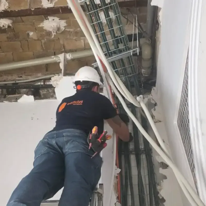 Obrero de la construcción con casco instalando cables en un espacio de techo sin terminar