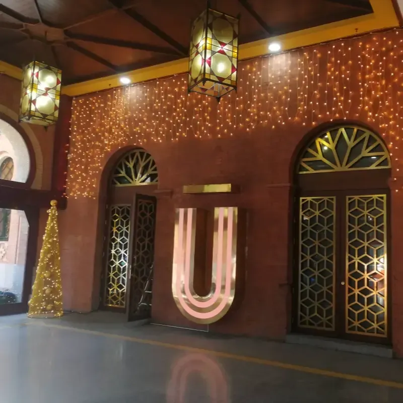 Entrada con iluminación tenue, luces de hadas cálidas, puertas decorativas y un letrero luminoso en forma de U.