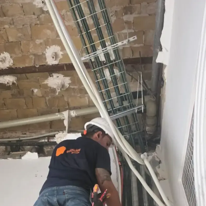 Un trabajador con casco inspecciona los cables del techo en una habitación parcialmente demolida.